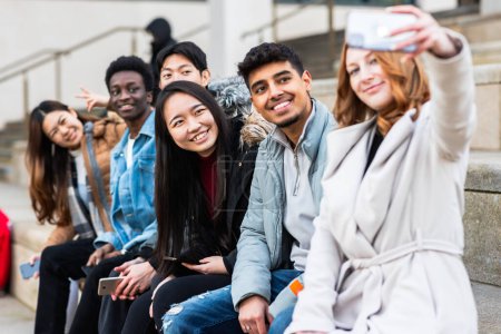 Foto de Multiracial people taking a selfie together and making funny faces - Happy friendship and diversity concepts with mixed race young best friends having fun in the city - Imagen libre de derechos