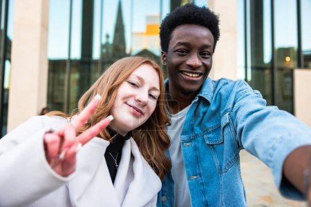 Foto de Pareja multiracial tomando una selfie juntos y sonriendo a la cámara - Felices conceptos de amistad y diversidad con la raza mixta jóvenes mejores amigos divertirse en la ciudad - Imagen libre de derechos