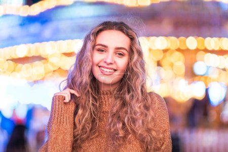 Foto de Retrato de mujer sonriente en el parque de atracciones mirando a la cámara y sonriendo - mujer joven divirtiéndose en una noche en la feria de la diversión - Imagen libre de derechos