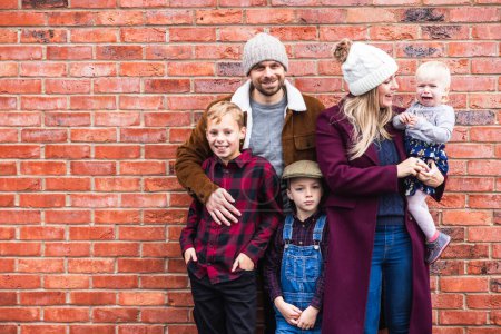 Photo for Happy family portrait with crying baby against brick wall - Candid beautiful young family with children enjoying time outdoors - Lifestyle and family concepts - Royalty Free Image