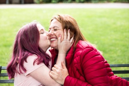Foto de Chica dando un beso encantador a su madre - Madre e hija compartiendo un buen momento juntos - Familia franca disparó en el parque con los padres mayores y la niña - Imagen libre de derechos