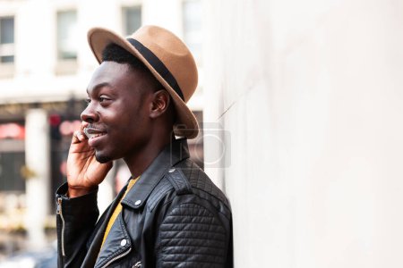 Foto de Hombre negro feliz hablando por teléfono y sonriendo - Joven de moda en Londres disfrutando de una conversación telefónica - Estilo de vida, tecnología y conceptos de comunicación - Imagen libre de derechos