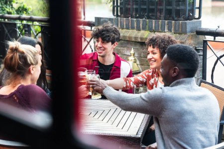 Foto de Amigos multirraciales felices disfrutando de la bebida juntos - Concepto de estilo de vida de amistad con los jóvenes que pasan tiempo juntos en el pub en Londres - Gente negra, asiática y caucásica - Imagen libre de derechos