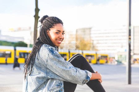 Téléchargez les photos : Une jeune femme noire souriante avec des tresses profite d'une journée ensoleillée en ville - Joyeux jeune femme en milieu urbain à Berlin - en image libre de droit