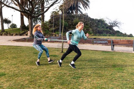 Téléchargez les photos : Femmes faisant de l'exercice au parc, renforçant l'exercice de course - deux belles jeunes femmes à Porto s'entraînant ensemble par une journée nuageuse - activités de plein air et sport - en image libre de droit