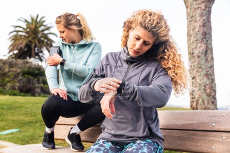 Foto de Mujeres revisando smartwatch y teléfono después del ejercicio - Dos mujeres jóvenes entrenando en Oporto, estilo de vida saludable y conceptos deportivos - Tecnología y conceptos de gadgets portátiles - Imagen libre de derechos