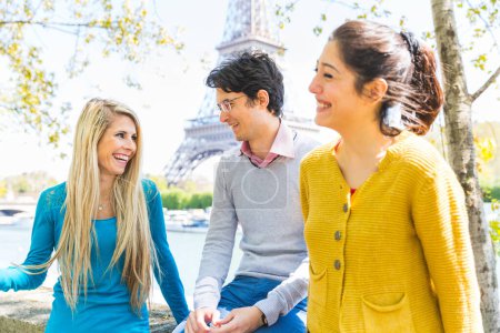 Foto de Tres alegres amigos disfrutando del tiempo juntos en un soleado parque en París junto al río Sena y la torre Eiffel - Amigos riendo y pasando tiempo al aire libre en París - Imagen libre de derechos