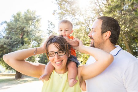 Téléchargez les photos : Des parents heureux embrassant leur bébé avec affection lors d'une sortie en famille - Joyeux famille profitant d'une journée ensoleillée dans le parc - en image libre de droit