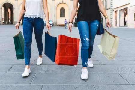 Foto de Dos mujeres paseando por las calles de la ciudad con coloridas bolsas de compras - Compras mejores amigos disfrutando de la terapia al por menor en Italia - Imagen libre de derechos