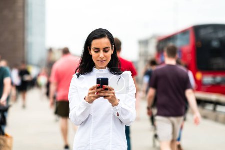 Foto de Mujer de negocios usando un teléfono inteligente en la ciudad - Hermosa mujer con camisa blanca escribiendo en un teléfono móvil - Ocupado camino y pavimento en el fondo - Imagen libre de derechos