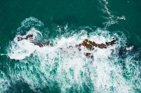 Photo for Top-down shot of turquoise ocean waves breaking against a rugged coast - Aerial view of crashing waves on rocky shoreline - Royalty Free Image