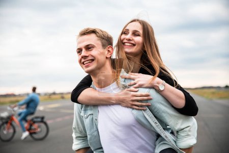 Happy couple having fun and enjoying a piggyback ride - Caucasian man and woman, best friends, sharing time together and laughing in Berlin at Tempelhof airport park - Friendship and happiness lifestyle concepts