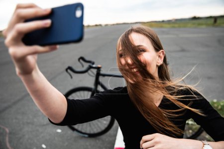 Téléchargez les photos : Femme heureuse prenant un selfie avec les cheveux ébouriffés devant le visage - Femme souriante caucasienne aux cheveux longs s'amusant à Berlin au parc de l'aéroport Tempelhof - concepts de bonheur et de style de vie - en image libre de droit