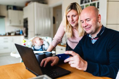 Foto de Familia haciendo compras en línea y tener un bebé recién nacido en la sala de estar - Conceptos de trabajo remoto, niños, paternidad, estilo de vida en el Reino Unido - Imagen libre de derechos