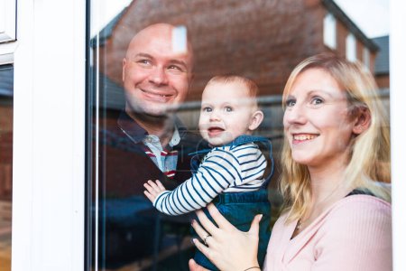 Téléchargez les photos : Heureux portrait de famille, souriant et regardant par la fenêtre - Heureux petit garçon avec mère et père profiter du temps ensemble et s'amuser - Style de vie et concepts de famille - en image libre de droit