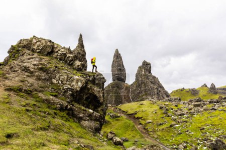 Man hiking in Scotland, Isle of Skye at the Old Man of Storr - Hiker climbing on rocks with the famous rock of the Isle of Skye on a cloudy  day - Travel and adventure concepts