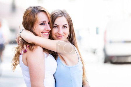 Téléchargez les photos : Des femmes heureuses en ville qui se sourient et se serrent dans leurs bras - Deux jeunes femmes caucasiennes qui s'amusent en ville pendant leurs achats - Meilleurs amis partageant des moments heureux ensemble - en image libre de droit