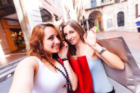 Téléchargez les photos : Femmes heureuses faisant du shopping et prenant un selfie en ville - Deux jeunes femmes caucasiennes s'amusent en ville tout en faisant du shopping - Meilleurs amis partageant des moments heureux ensemble - en image libre de droit