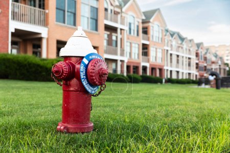 Foto de Vibrante boca de incendios roja frente a casas adosadas residenciales con césped verde en Nueva Jersey - boca de incendios roja en el barrio suburbano - Imagen libre de derechos