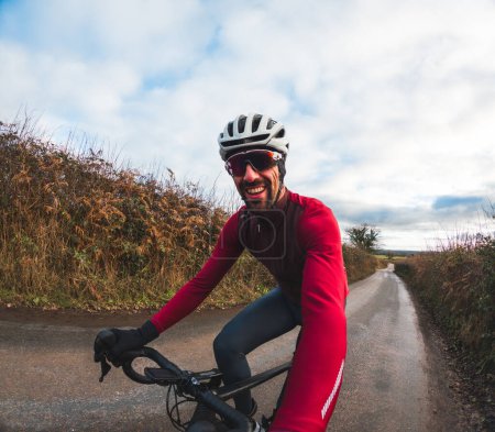 Téléchargez les photos : Rayonnement homme en équipement de vélo promenades le long d'une voie rurale sereine - Heureux cycliste profiter d'une promenade sur la route de campagne et de prendre un selfie - en image libre de droit