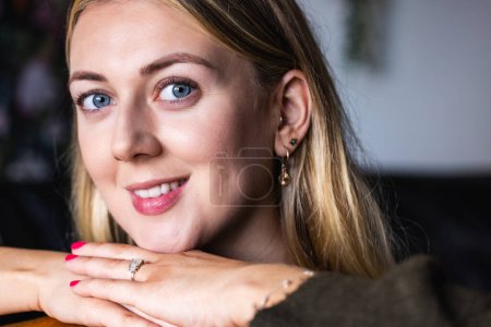 Photo for Close-up of a joyful blonde woman with clear blue eyes, casually resting her chin on her hands - Smiling woman with sparkling eyes close-up portrait - Royalty Free Image