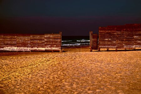 Téléchargez les photos : Clôture en planches de bois sur la rive israélienne de la mer Méditerranée au coucher du soleil. Le mur séparant la partie religieuse masculine et féminine de la plage en Israël - en image libre de droit