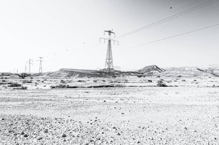 Téléchargez les photos : Lignes électriques sur pylônes dans le paysage du Moyen-Orient. Collines rocheuses du désert du Néguev en Israël en noir et blanc. - en image libre de droit