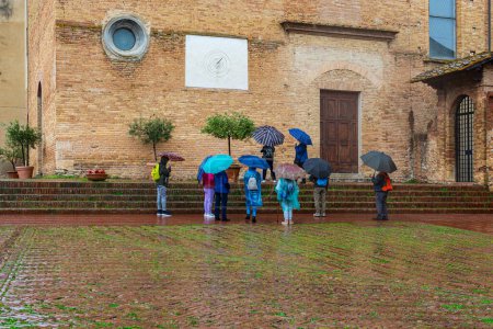 Foto de Turistas frustrados bajo la lluvia con sombrillas viendo los lugares de interés de San Gimignano en Italia - Imagen libre de derechos