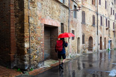 Foto de Turistas frustrados bajo la lluvia con sombrillas viendo los lugares de interés de San Gimignano en Italia - Imagen libre de derechos
