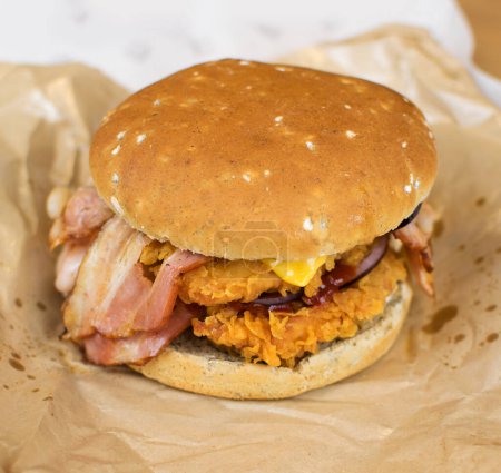 Téléchargez les photos : Burger avec poulet pané et bacon sur papier. Aliments gras malsains. - en image libre de droit