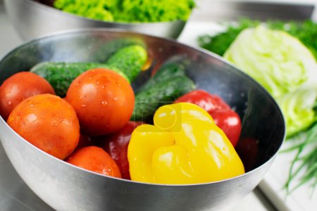 Téléchargez les photos : Poivrons, tomates et concombres frais lavés dans une assiette en métal. Laitue, chou et autres légumes verts sont en arrière-plan. - en image libre de droit