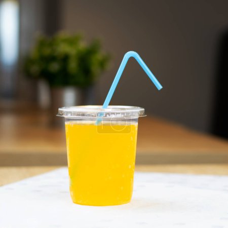Téléchargez les photos : Coupe en plastique avec boisson orange et paille sur la table dans le café - en image libre de droit