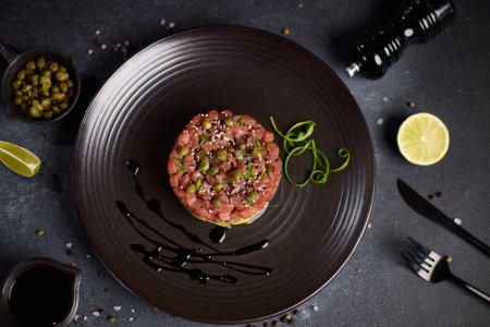 Tuna and avocado tartare with sesame seeds and capers on a dark ceramic plate.