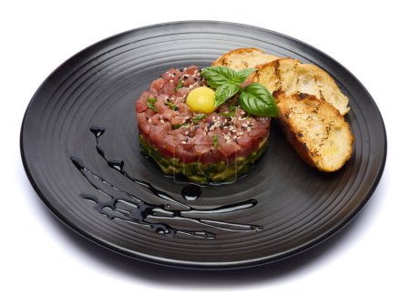 Tuna and avocado tartare with sesame seeds, capers and egg yolk on a dark ceramic plate with baguette bread crouton chips. 4K DCI