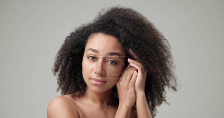 Concepto de belleza y salud: hermosa mujer afroamericana con cabello rizado afro y piel limpia y saludable sobre fondo gris del estudio posando y mirando a la cámara.