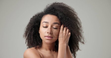 Concepto de belleza y salud: hermosa mujer afroamericana con cabello rizado afro y piel limpia y saludable sobre fondo gris del estudio posando y mirando a la cámara.