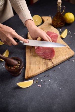 Woman cut tuna steak into slices on a wooden cutting board at domestic kitchen cooking tuna carpaccio.