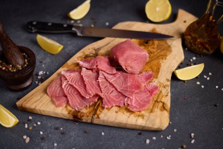 Woman cut tuna steak into slices on a wooden cutting board at domestic kitchen cooking tuna carpaccio.