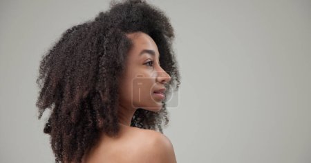 Concepto de belleza y salud: hermosa mujer afroamericana con cabello rizado afro y piel limpia y saludable en el fondo del estudio gris posando y mirando a la cámara. Foto de alta calidad