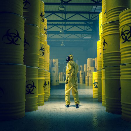 Foto de Man in yellow protective suit in warehouse with metal drums with radioactive and chemical waste. - Imagen libre de derechos