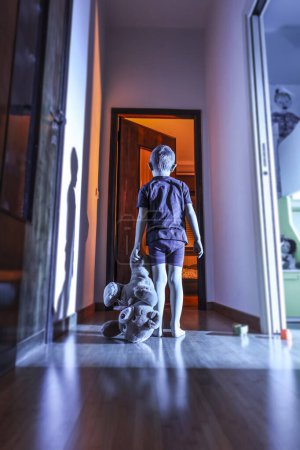 Téléchargez les photos : Enfant avec ours en peluche dans un lieu domestique, nuit et atmosphère mystérieuse - en image libre de droit