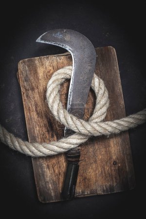 Photo for Old billhook wrapped with thick rope on a wooden background - Royalty Free Image