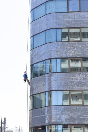 Photo for Worker abseils with a rope to carry out maintenance on a building - Royalty Free Image