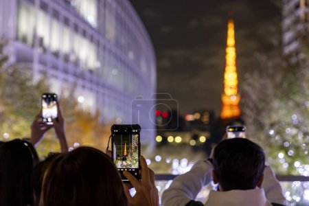 Photo for Tourists take a smartphone photo of the Tokyo tower at night - Royalty Free Image