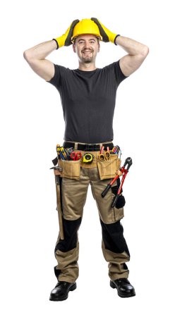 Téléchargez les photos : Travailleur souriant en casque dur et ceinture d'outils debout sur un fond blanc - en image libre de droit