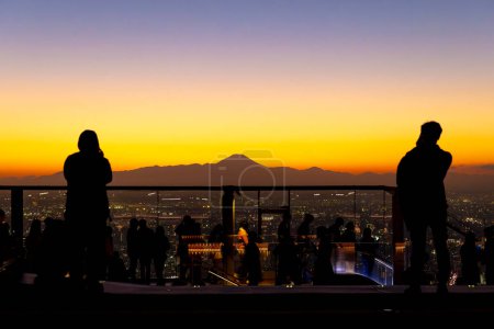Foto de La gente admira el paisaje urbano de Tokio contra una puesta de sol vibrante, con horizonte de silueta de montaña Fuji - Imagen libre de derechos
