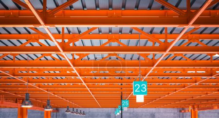Foto de Interior de un almacén con llamativas vigas de acero naranja y señales de estación numeradas - Imagen libre de derechos