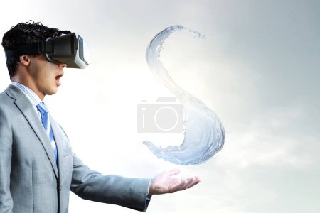 Photo for Man wearing virtual reality goggles holding a splash of clean water. Mixed media - Royalty Free Image