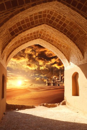 Antiguo arco a la entrada del desierto. Vista de dunas de arena y fabulosa ciudad perdida a través del arco de piedra. Hermoso paisaje desértico con dunas de arena y mítico castillo oriental sobre fondo de cielo al atardecer