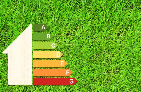 Foto de Vista superior de la tabla de eficiencia energética de la textura de cartón en hierba verde. Casa de papel ecológico y símbolo de eficiencia energética y hierba. Clase de energía, ir verde, bioenergética y ecología concepto - Imagen libre de derechos
